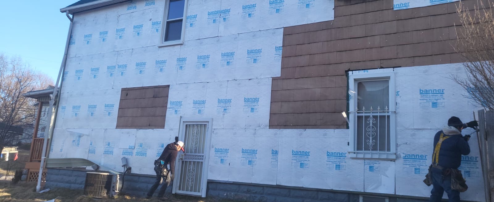 Crew installing house wrap after removing old siding from a two-story home