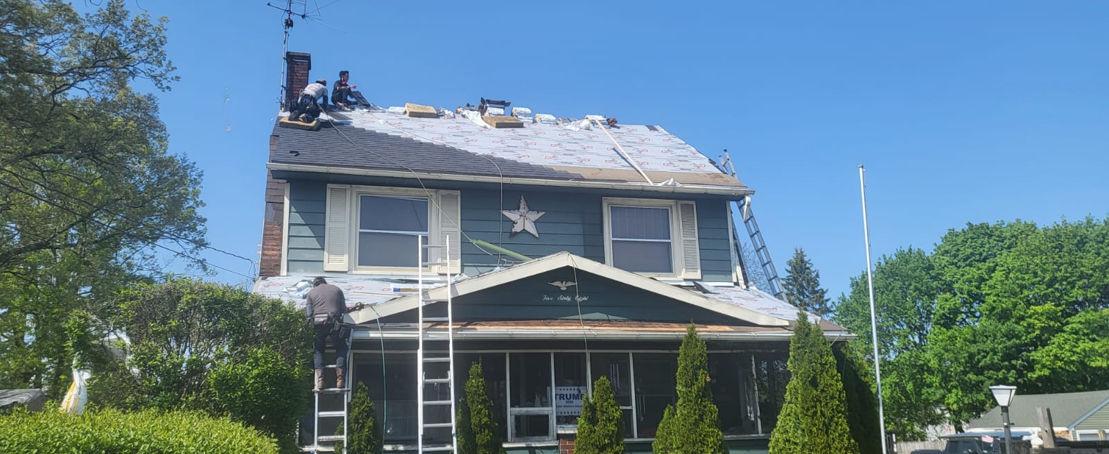 Roofing crew installing underlayment and shingles on a two-story home