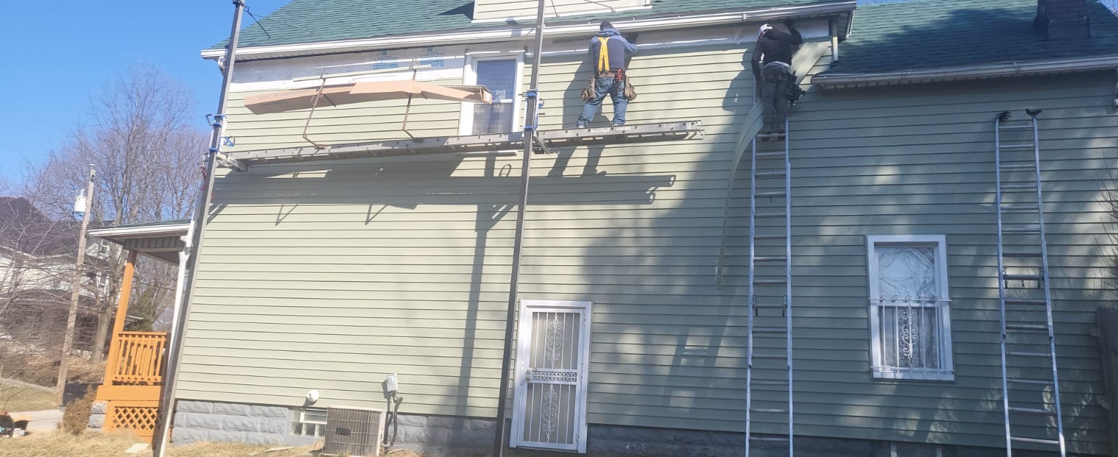 Two installers fitting new green vinyl siding and trim on a home